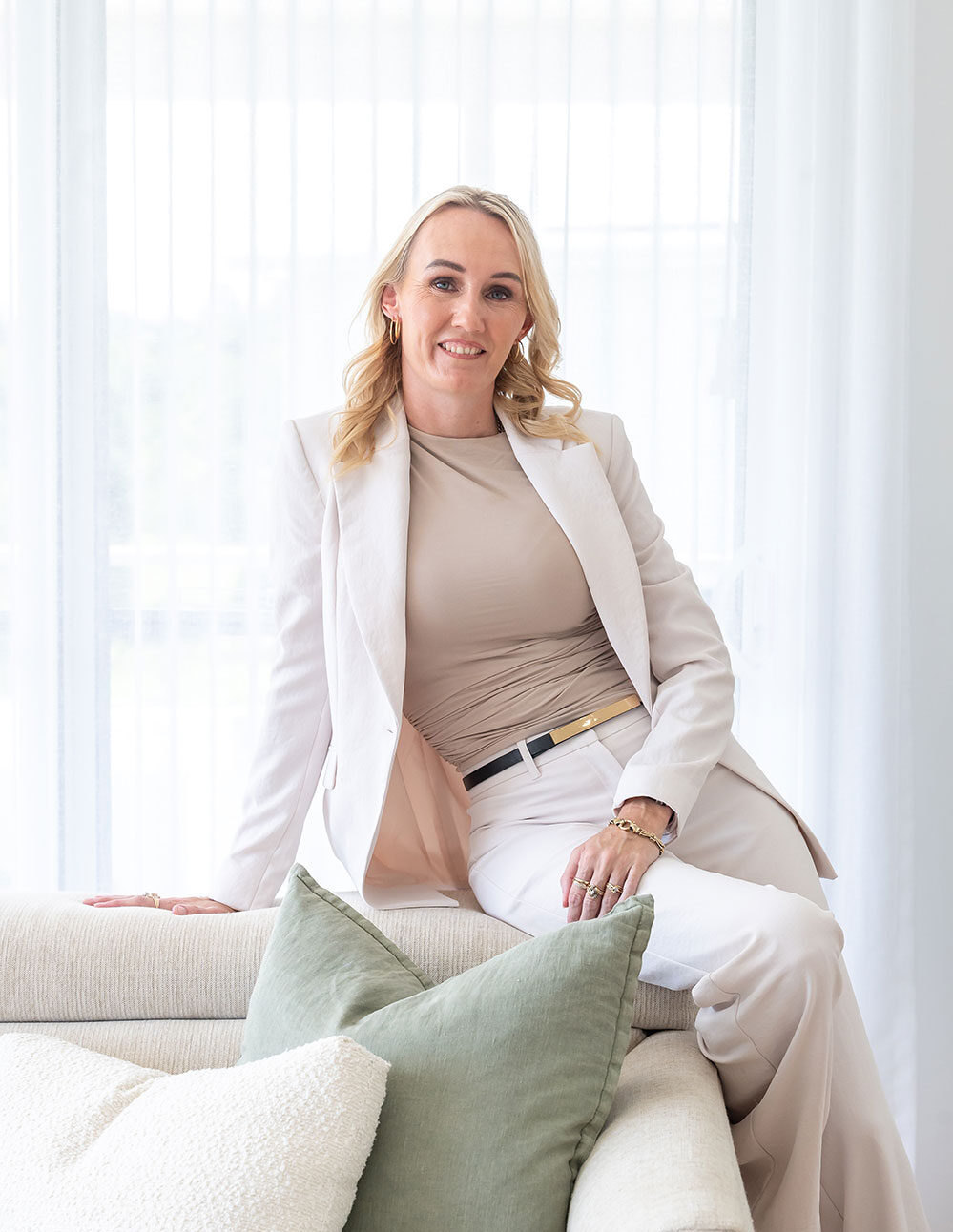 Professional NDIS service manager, Zoe Fuller, in a white suit, sitting comfortably on a sofa, ready to assist clients.